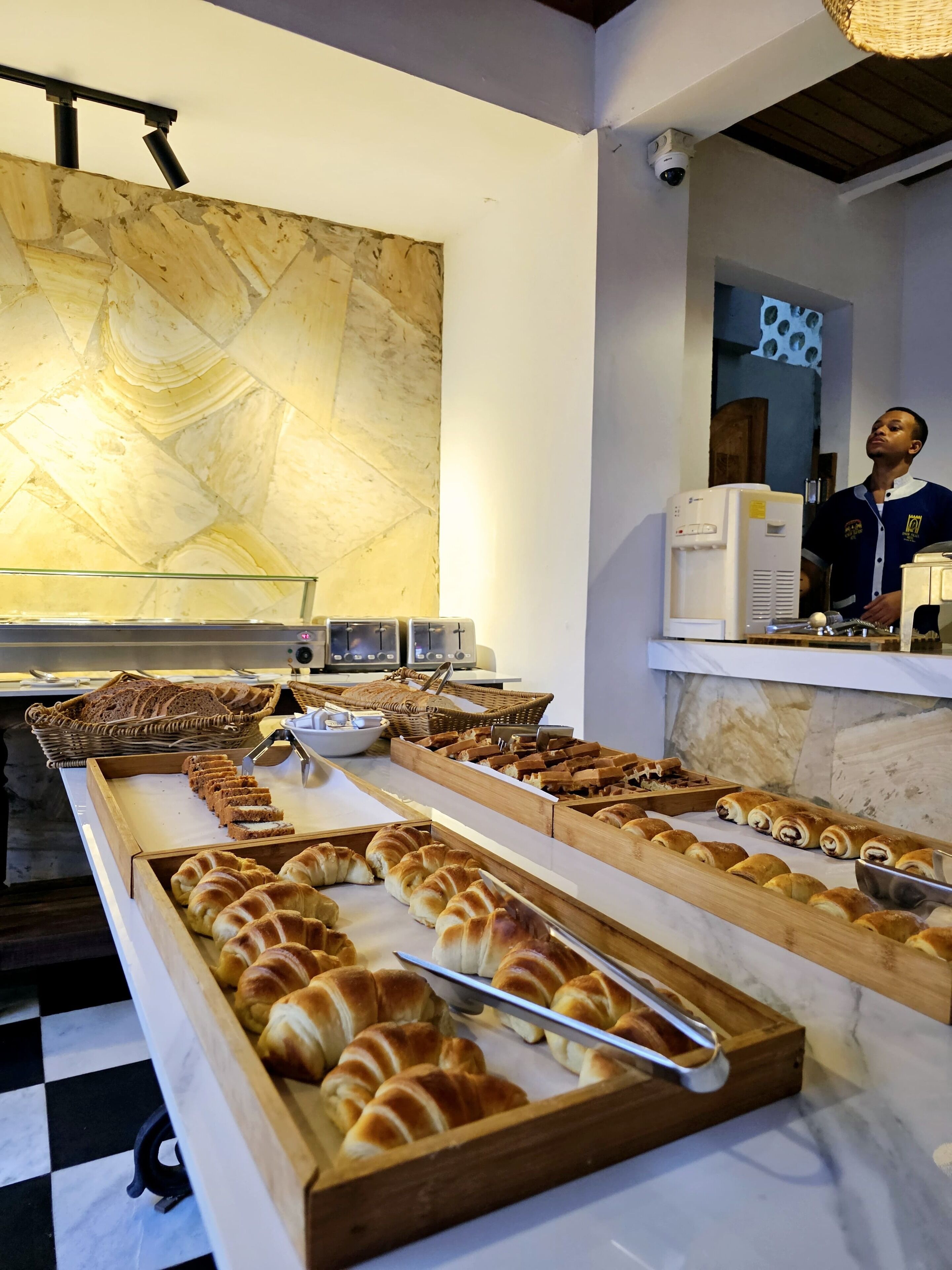 A breakfast buffet with various pastries and bread, a security camera, and a person in uniform.