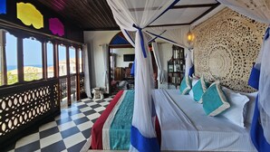 A room with a checkered floor, a bed with white and blue bedding, a canopy bed, and a view of the sea.