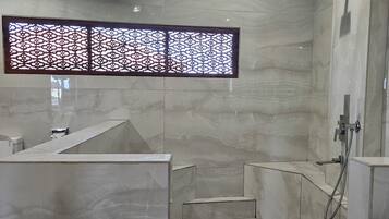 Zona de dutxa moderna amb sostre de fusta, una finestra decorativa i un paviment de marbre.