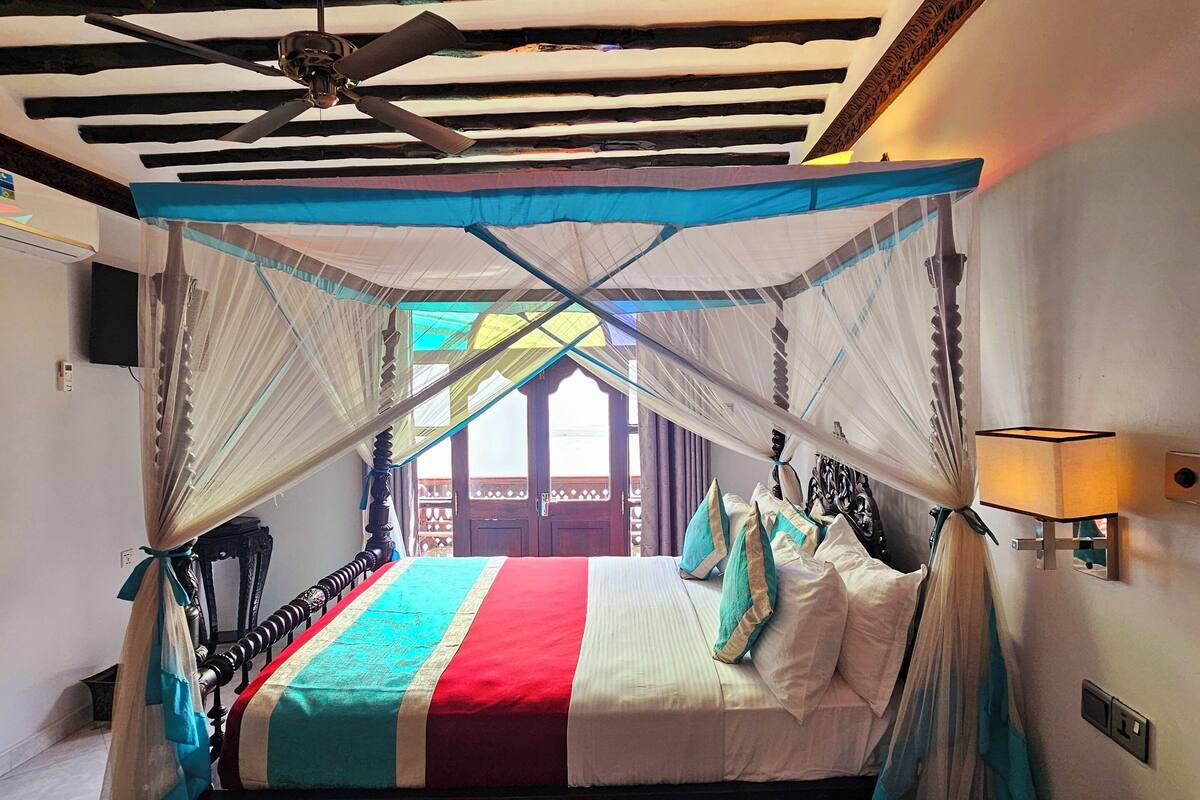 A bed with a canopy, a ceiling fan, and a view of the outside.