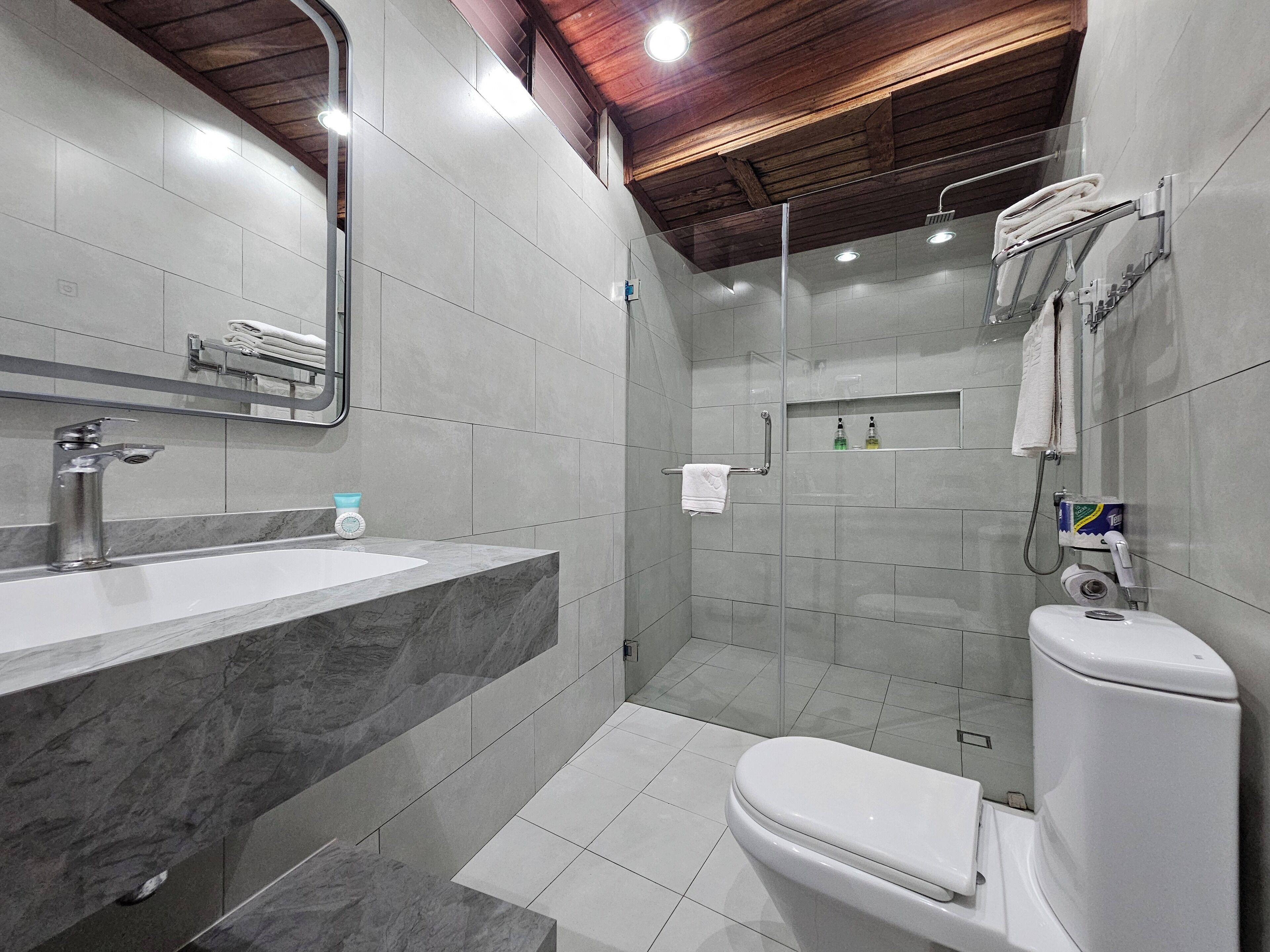 Un baño moderno con lavamanos de mármol, inodoro y cabina de ducha con paredes de vidrio.