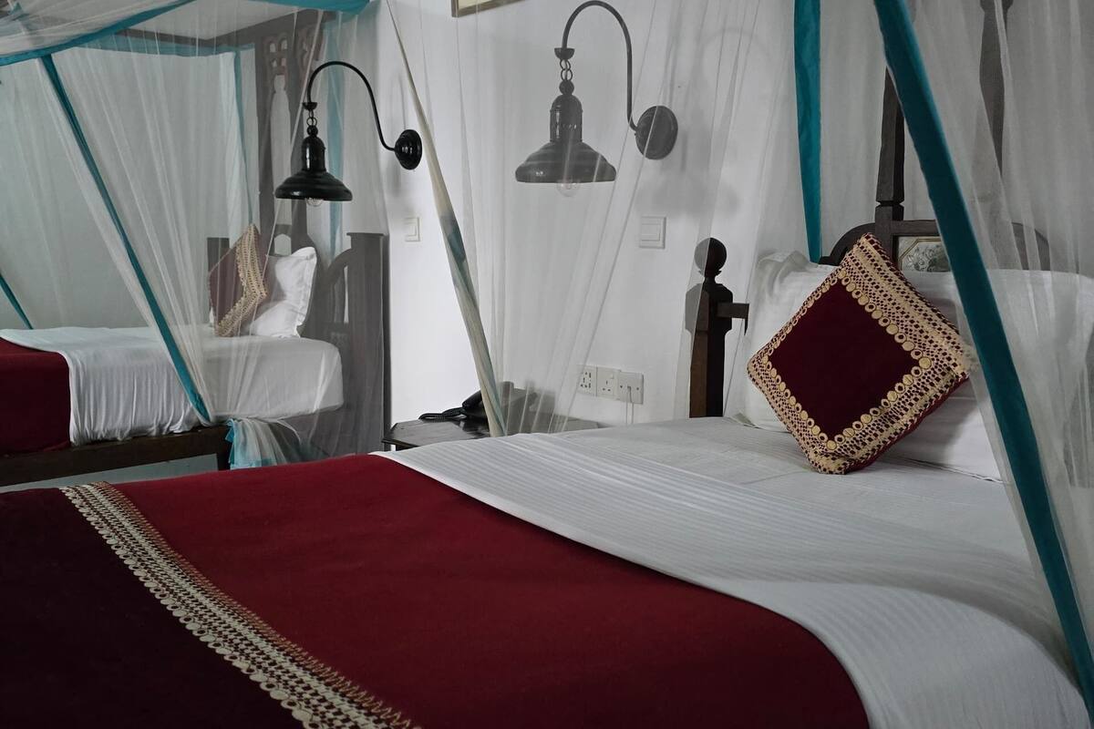 A room with a bed under a canopy, a bedside table, a lamp, and a wall-mounted light fixture.
