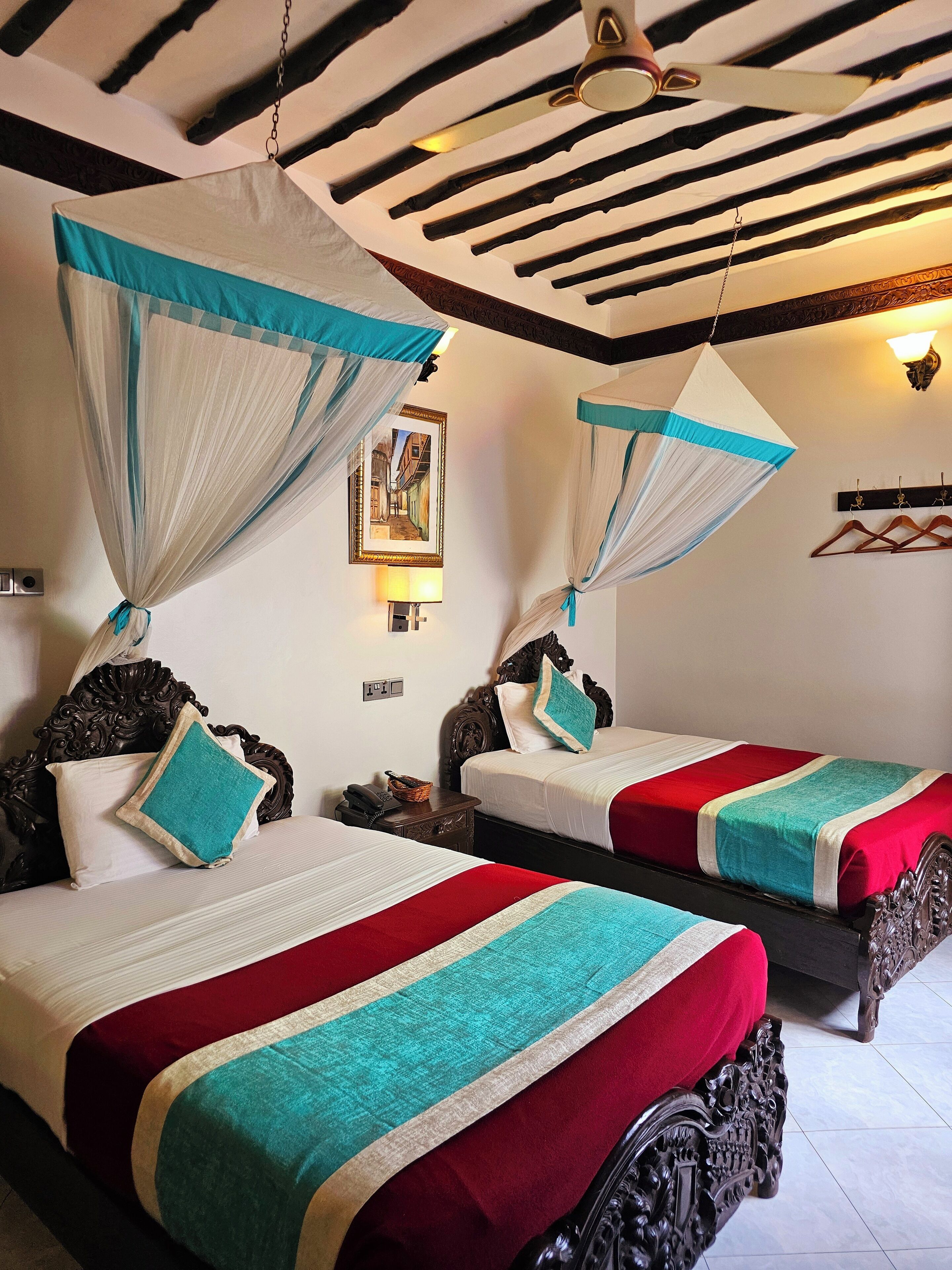 A hotel room with two beds, each with a canopy and red, white, and teal bedding.