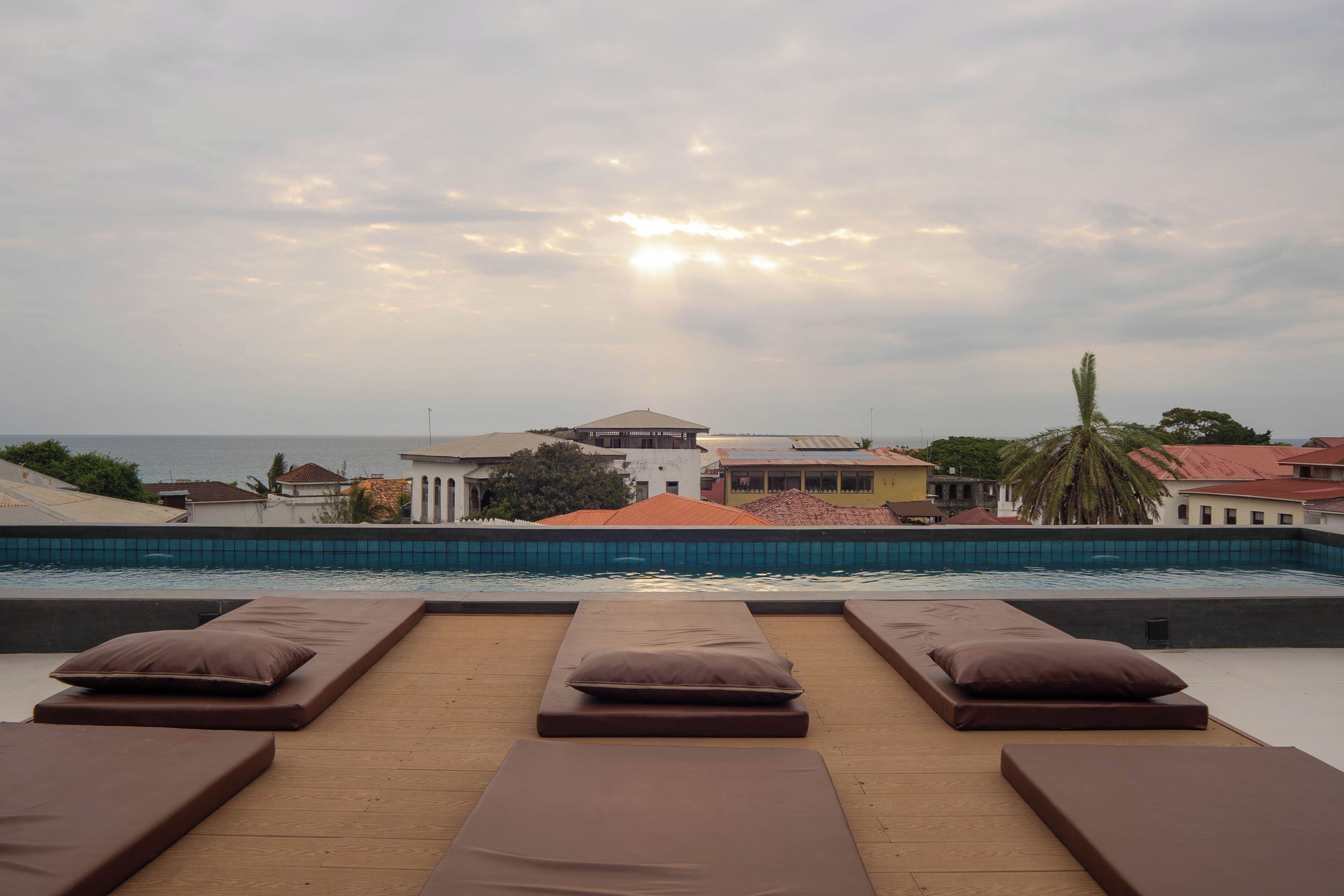 A poolside area with sun loungers and a view of the sea and buildings.