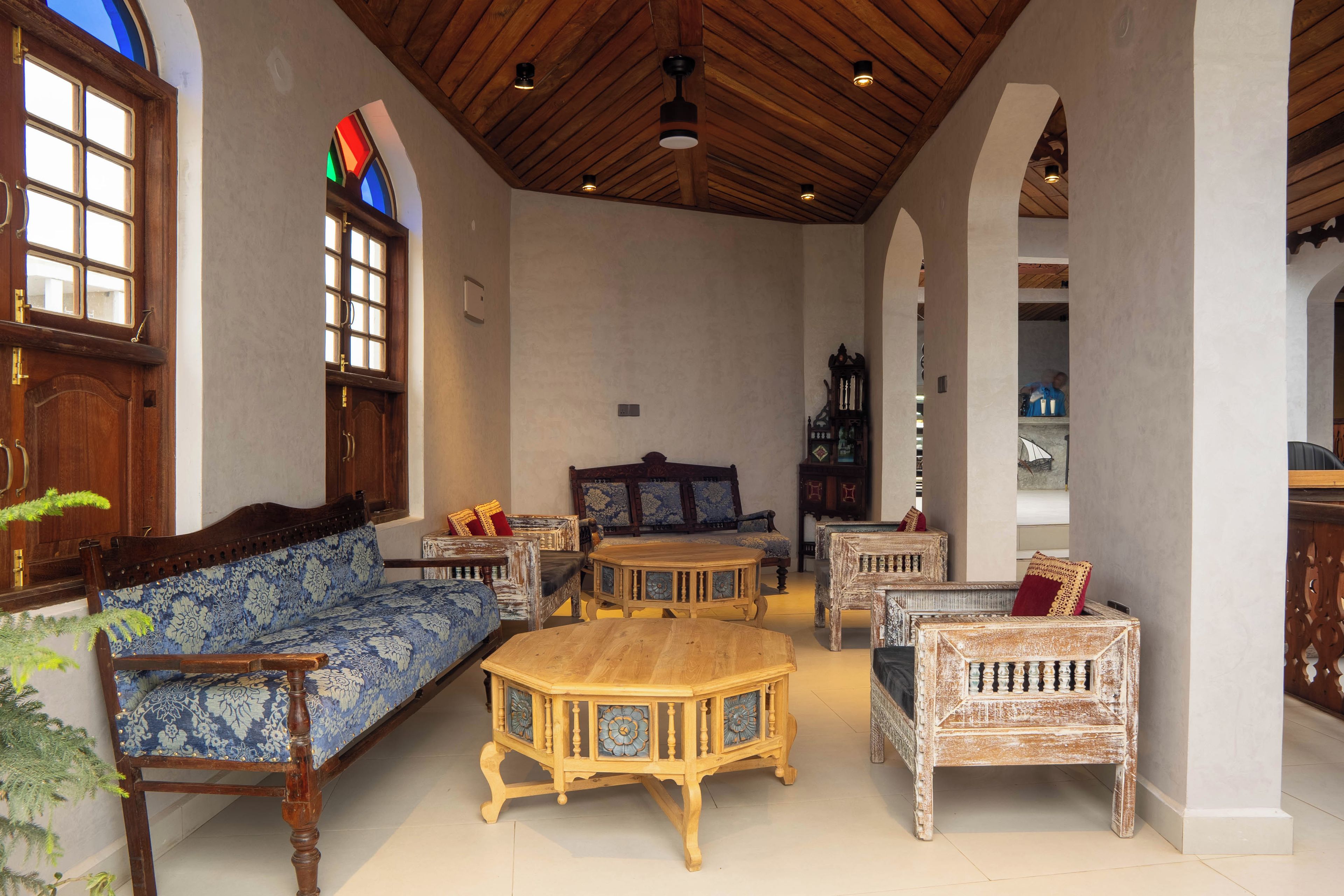 A spacious room with a high wooden ceiling, a large window with stained glass, and a variety of wooden furniture including sofas and tables.