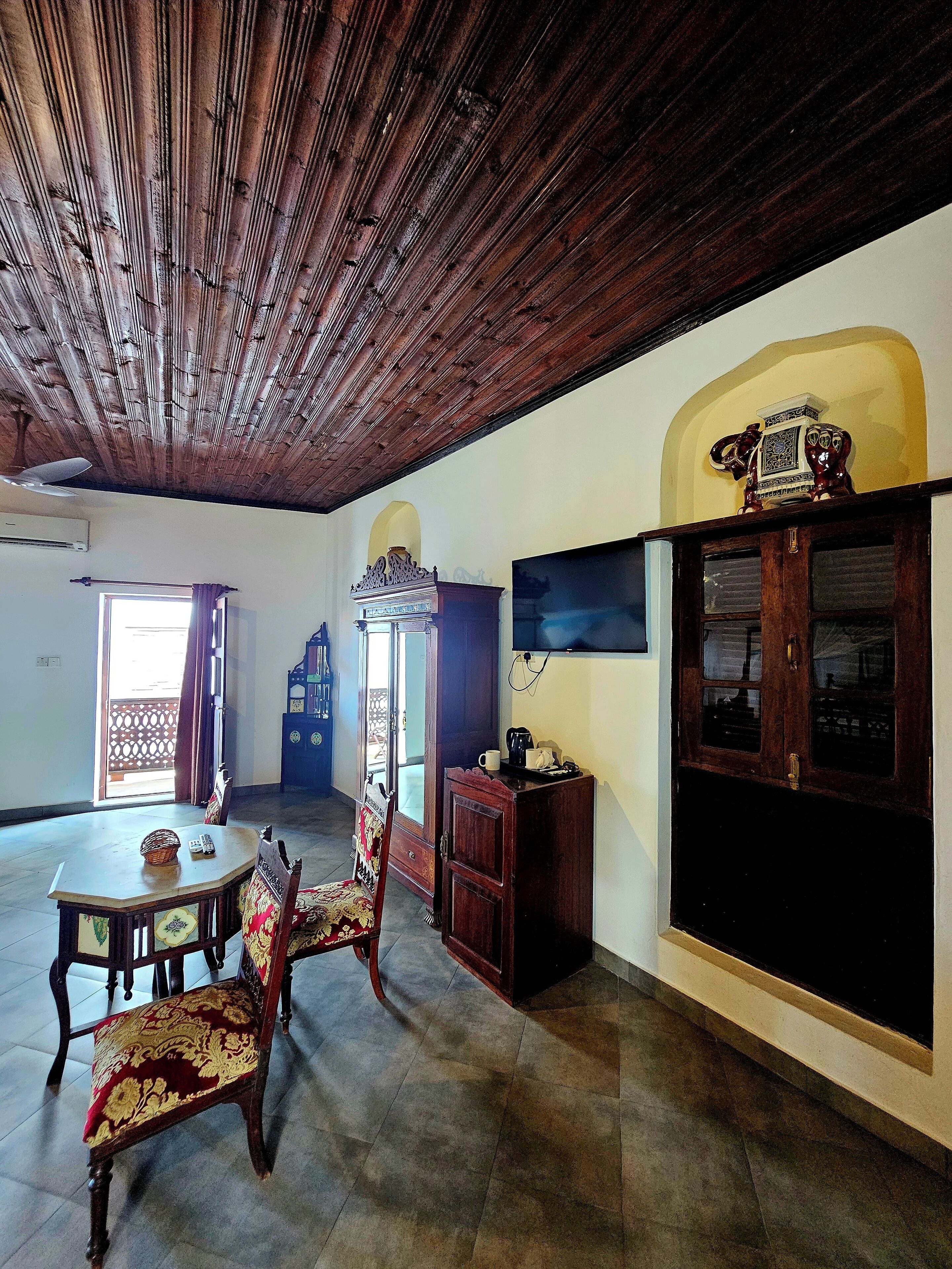 A room with a wooden ceiling, a dining table with chairs, a cabinet, and a television.