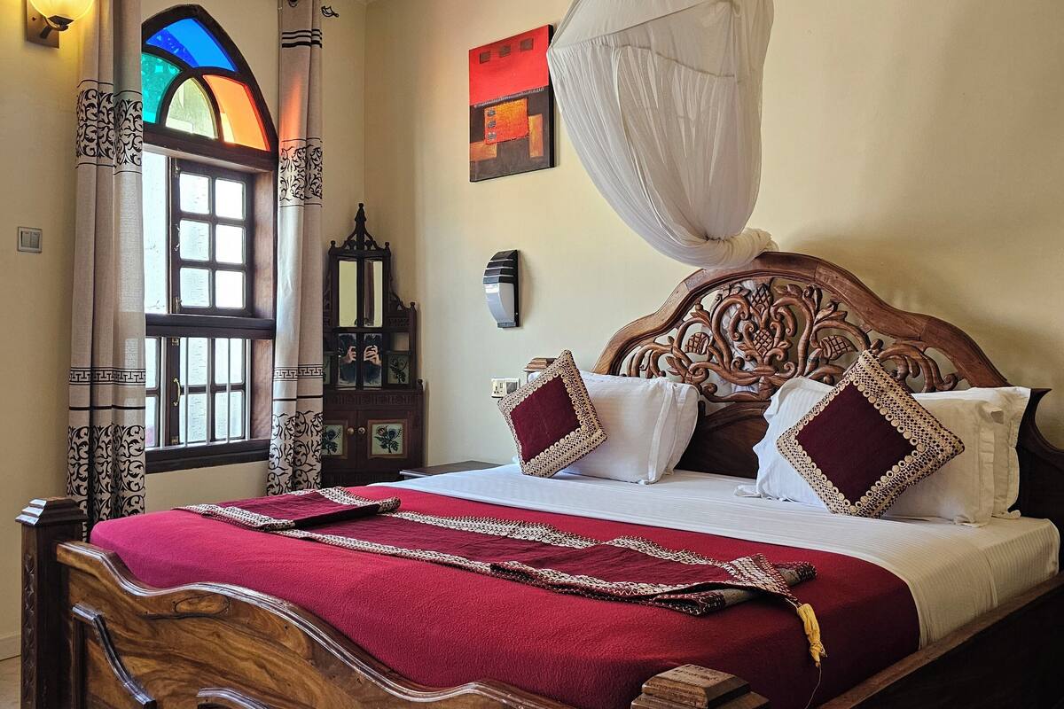 A wooden four-poster bed with a canopy, a red bedspread, and decorative pillows.