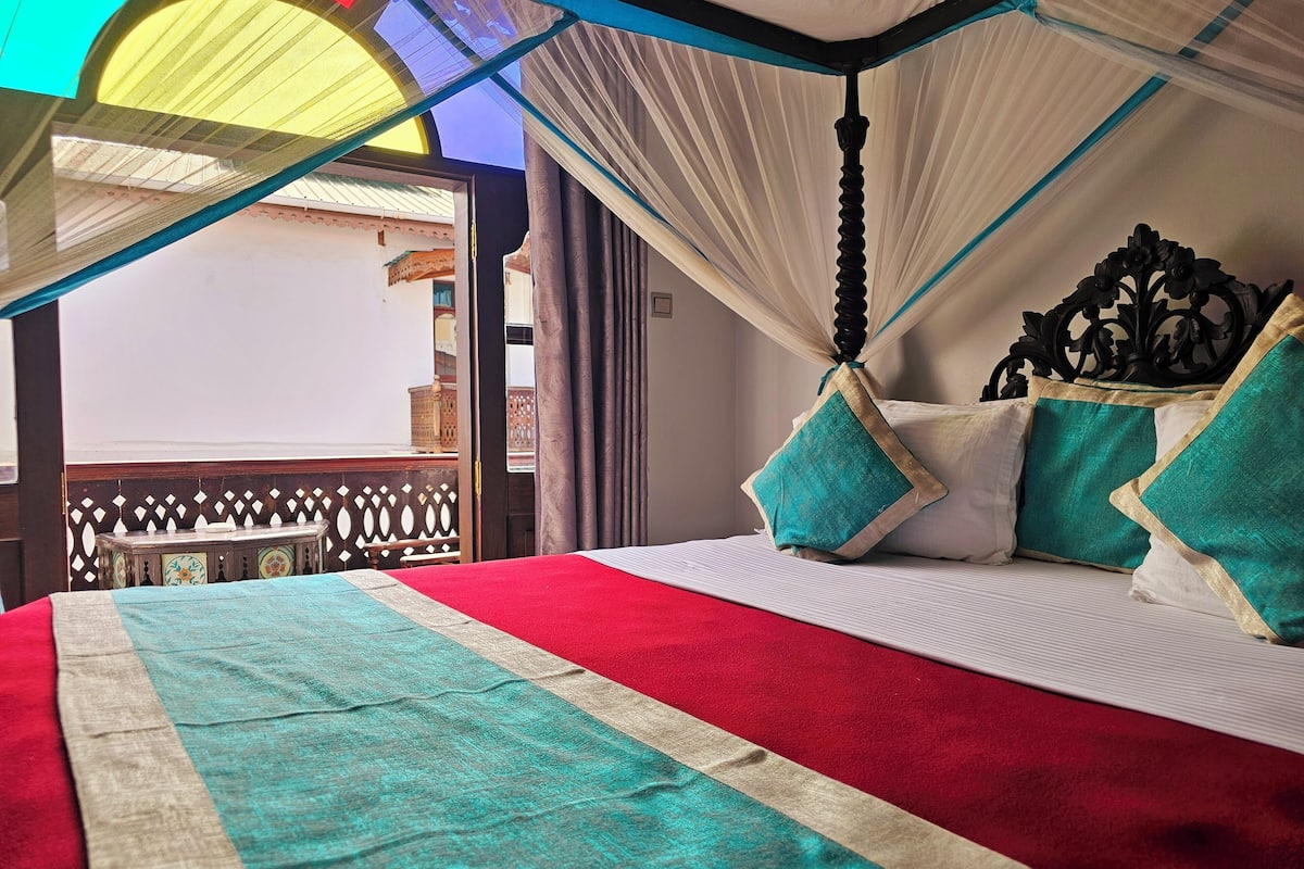 A bed with a red and white striped bedspread, teal pillows, and a canopy.