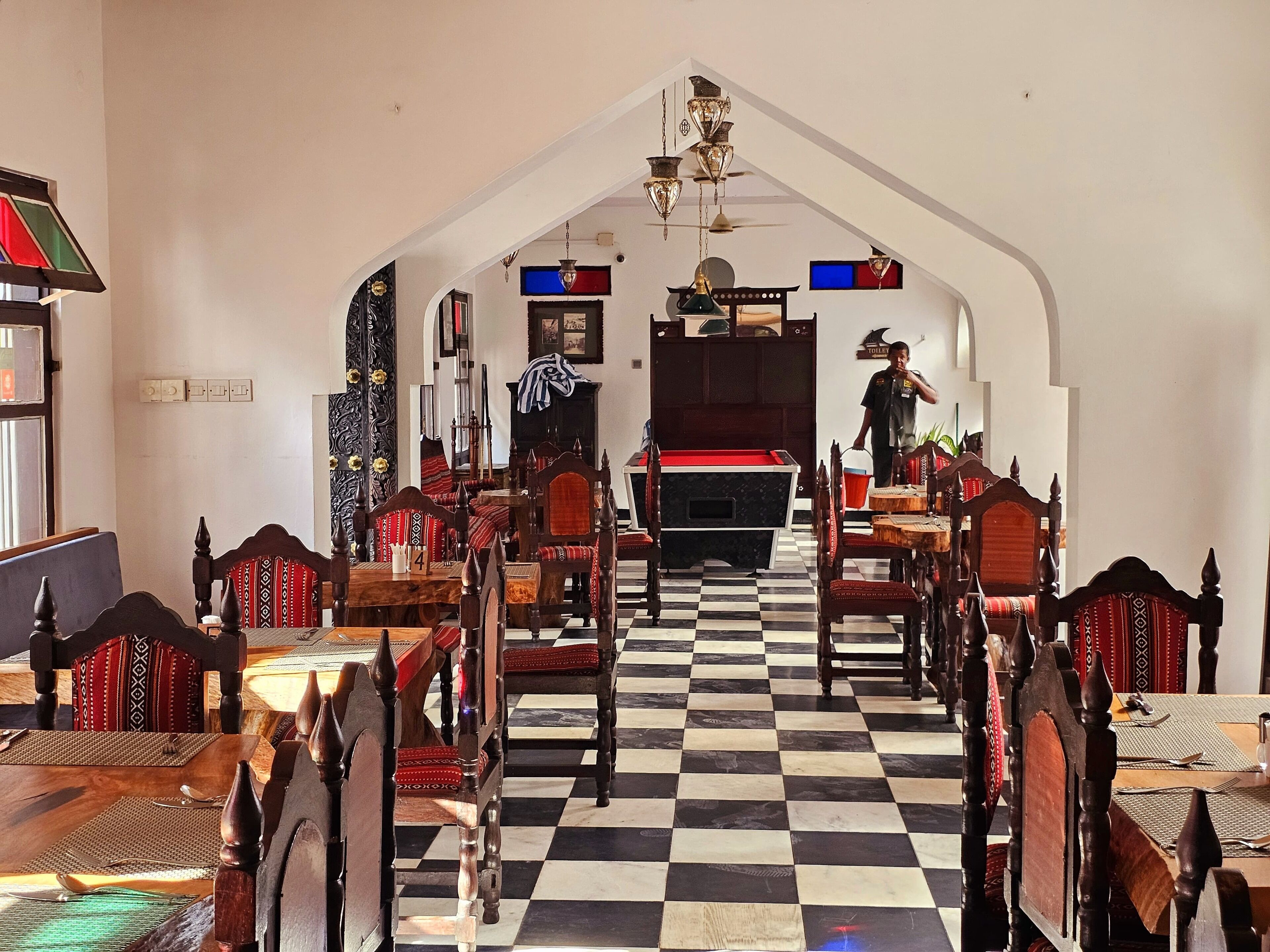 A hotel lobby with a checkered floor, wooden furniture, and a staircase leading to the upper floor.