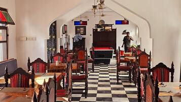 A hotel lobby with a checkered floor, wooden furniture, and a staircase leading to the upper floor.