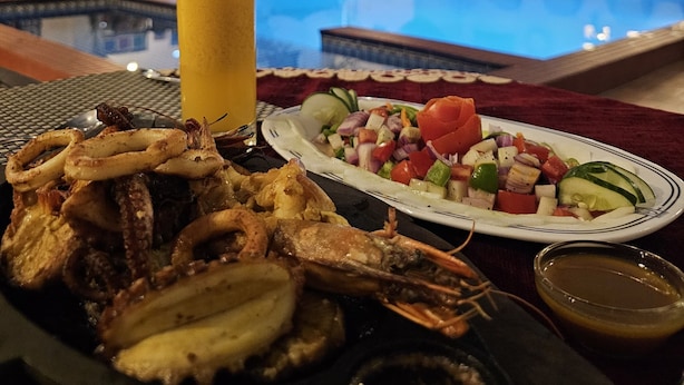 A dining table with seafood, a glass of orange juice, and a pool in the background.