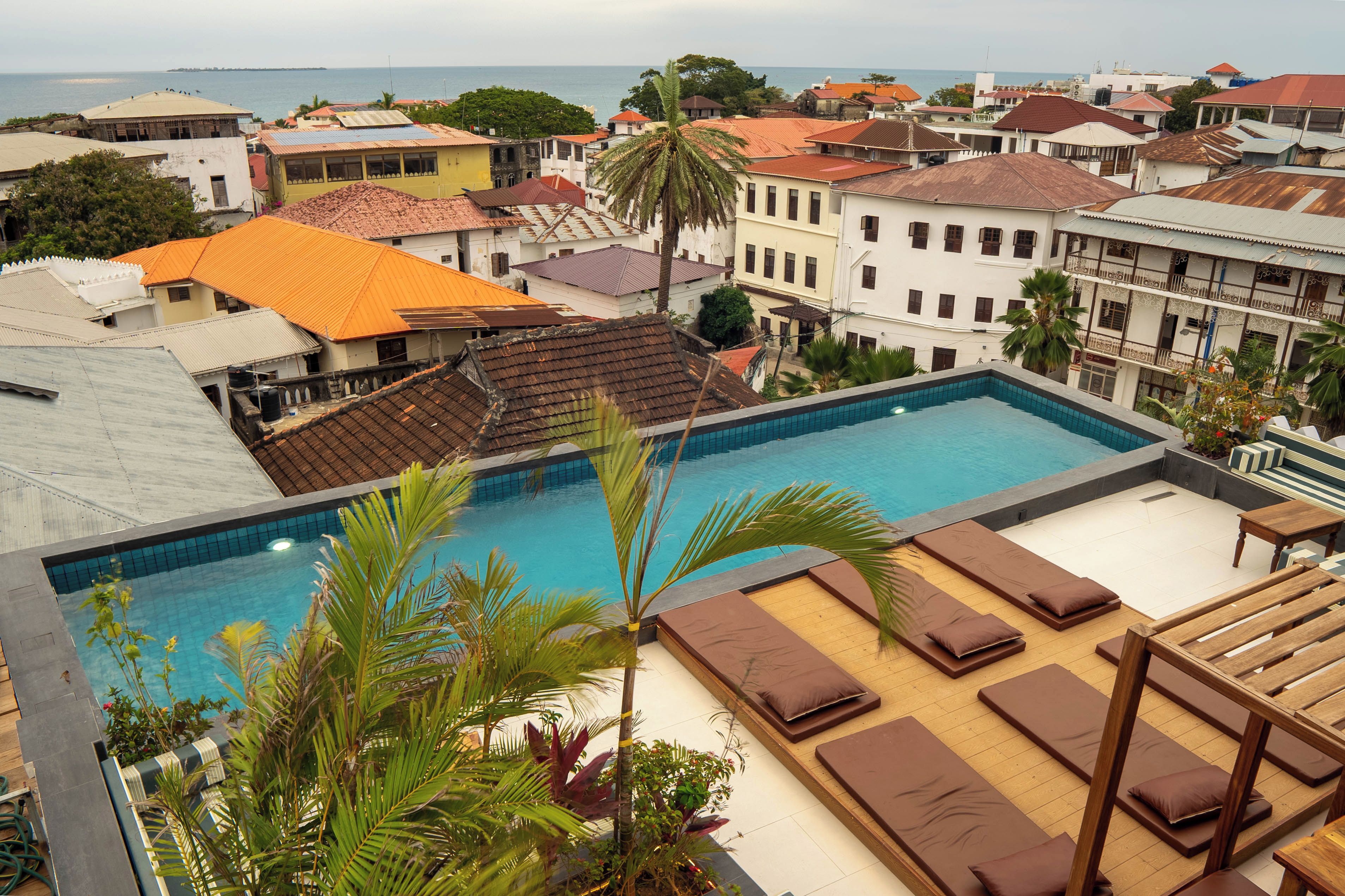 A rooftop pool with lounge chairs and a view of a coastal town.