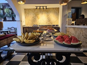 A buffet table with various food items, a marble wall, and a seating area with a checkered floor. - Dhow Palace Hotel (Zanzibar Town)