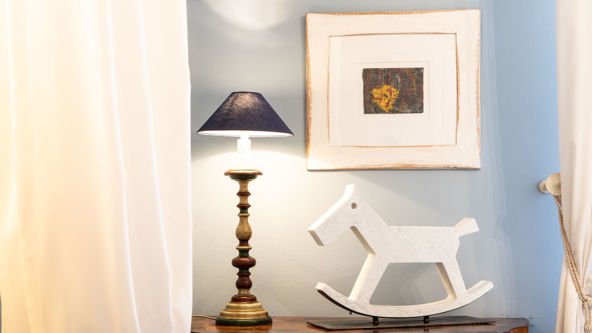 A room with a lamp, a framed picture, and a rocking horse.