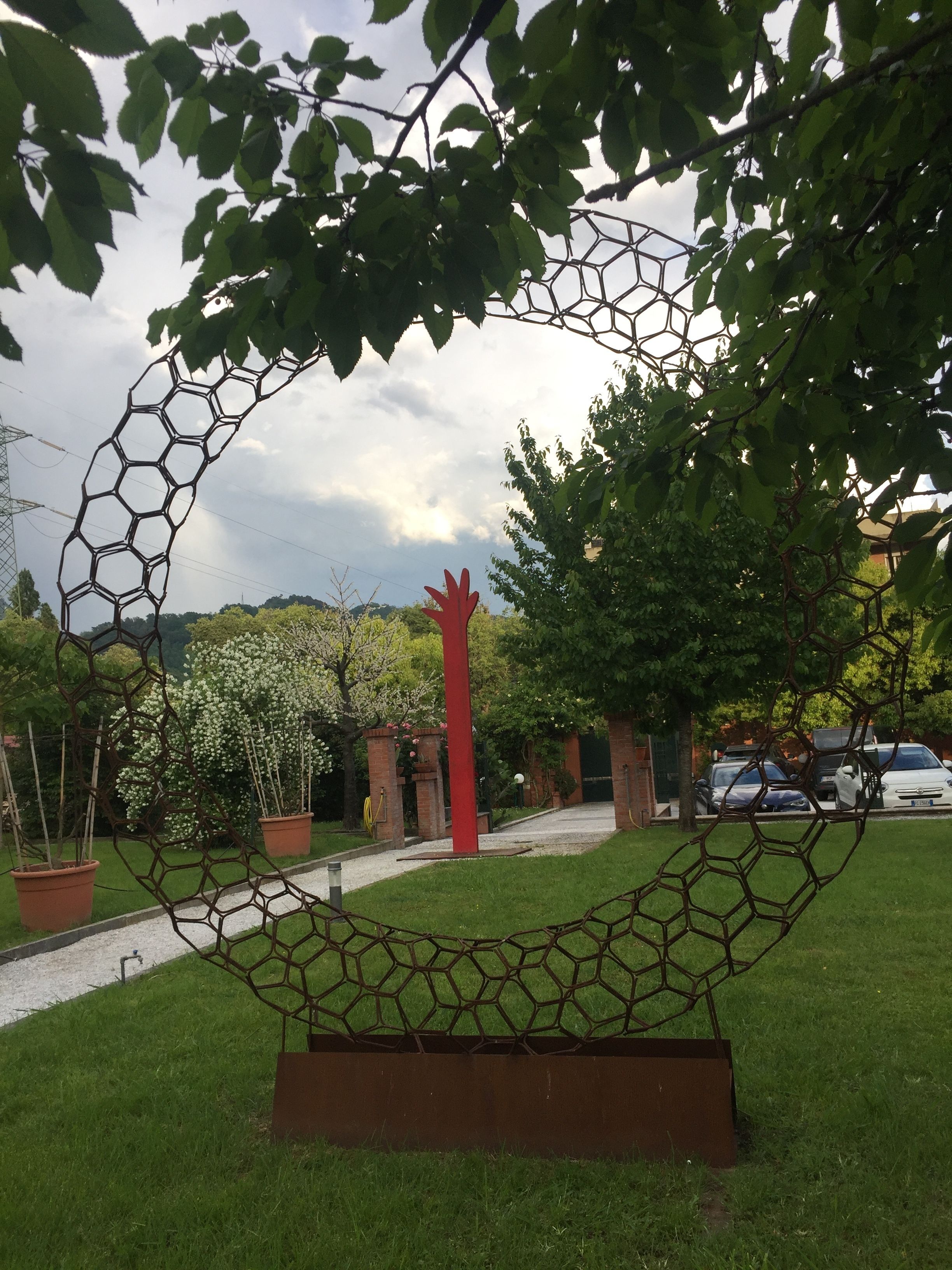 Ein Garten mit einer sechseckigen Metallskulptur, Blumentöpfen und einem Pflasterweg.