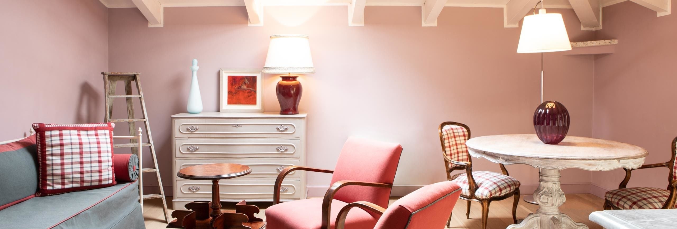 A cozy room with a sofa, chairs, a small table, a dresser, and a lamp.