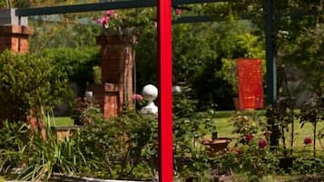 Uma escultura vermelha num jardim com um muro de tijolos e plantas floridas ao fundo.