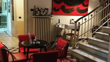 Un comedor con alfombra roja, una mesa negra y sillas rojas. Se observa una escalera con barandilla blanca y una pared roja con un cuadro abstracto en negro.