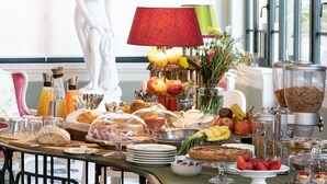 A breakfast buffet with various food items, a statue, and a large window in the background. - Villa Belverde (Carrara)