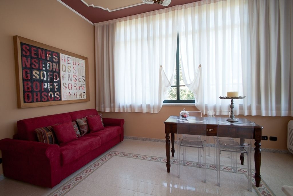Una sala de estar con un sofá rojo, una mesa de madera con una lámpara y una ventana con cortinas de gasa.