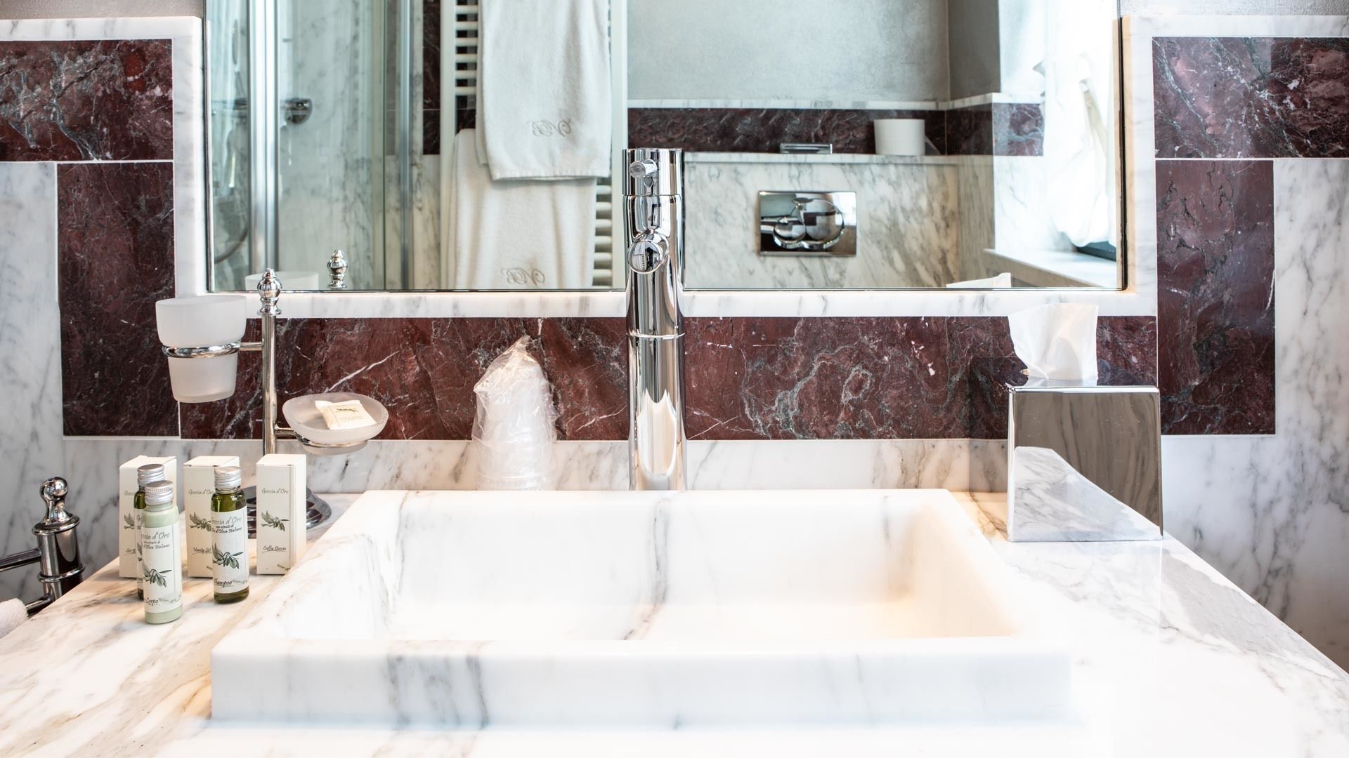 A bathroom with a large marble sink, a mirror, and toiletries on the counter.