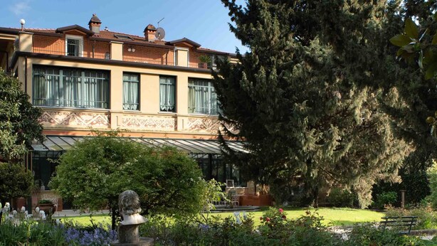 A building with a traditional architectural style, featuring a balcony and a garden with a statue and various plants. - Villa Belverde (Carrara)