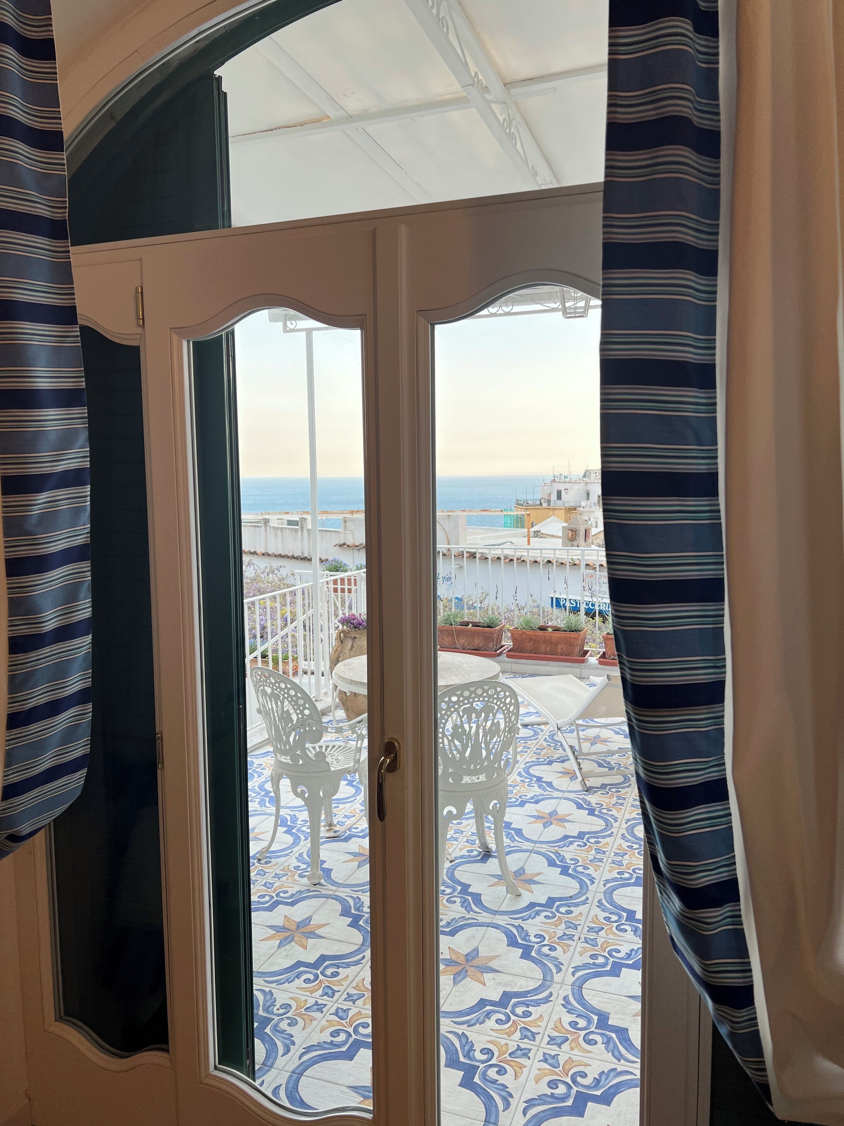 A room with a view of the sea, a patterned floor, and a door with curtains.