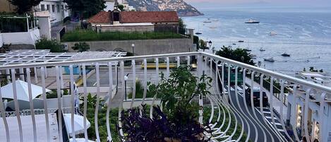 Un balcón con una mesa y sillas de metal blanco, con vistas a una zona costera con edificios y barcos.
