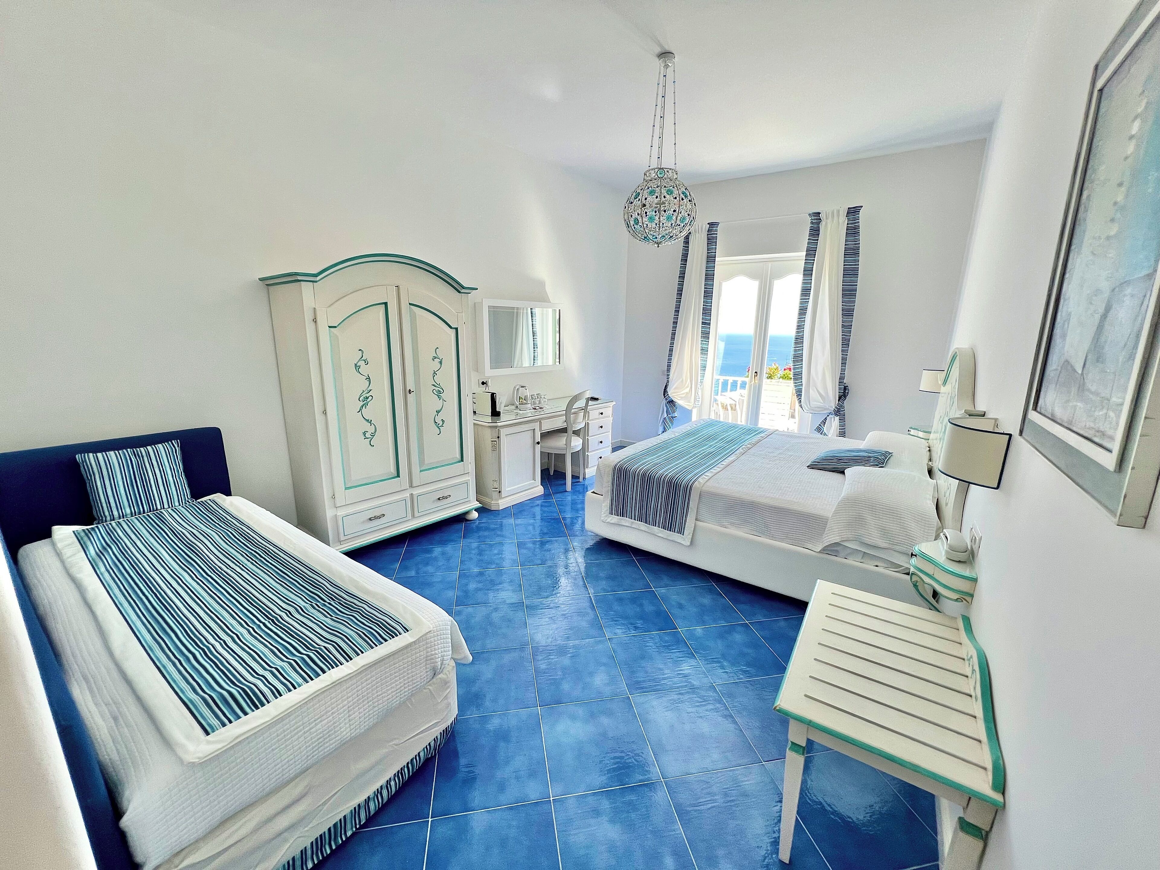 A hotel room with two beds, a vanity, and a view of the sea.