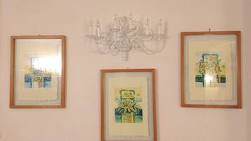 Three framed artworks on a wall, a chandelier, and a window with blinds.