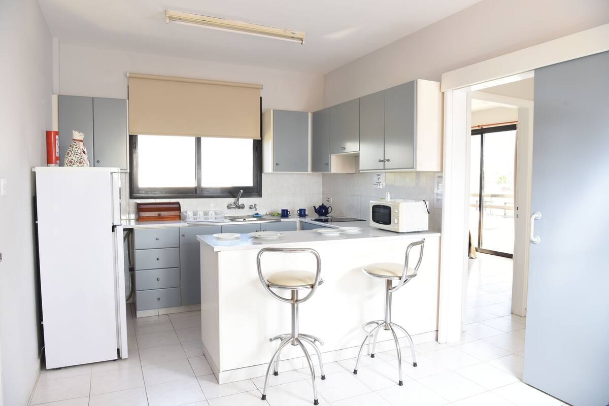 Una cocina moderna con una isla central, dos taburetes de bar, un refrigerador y un microondas.