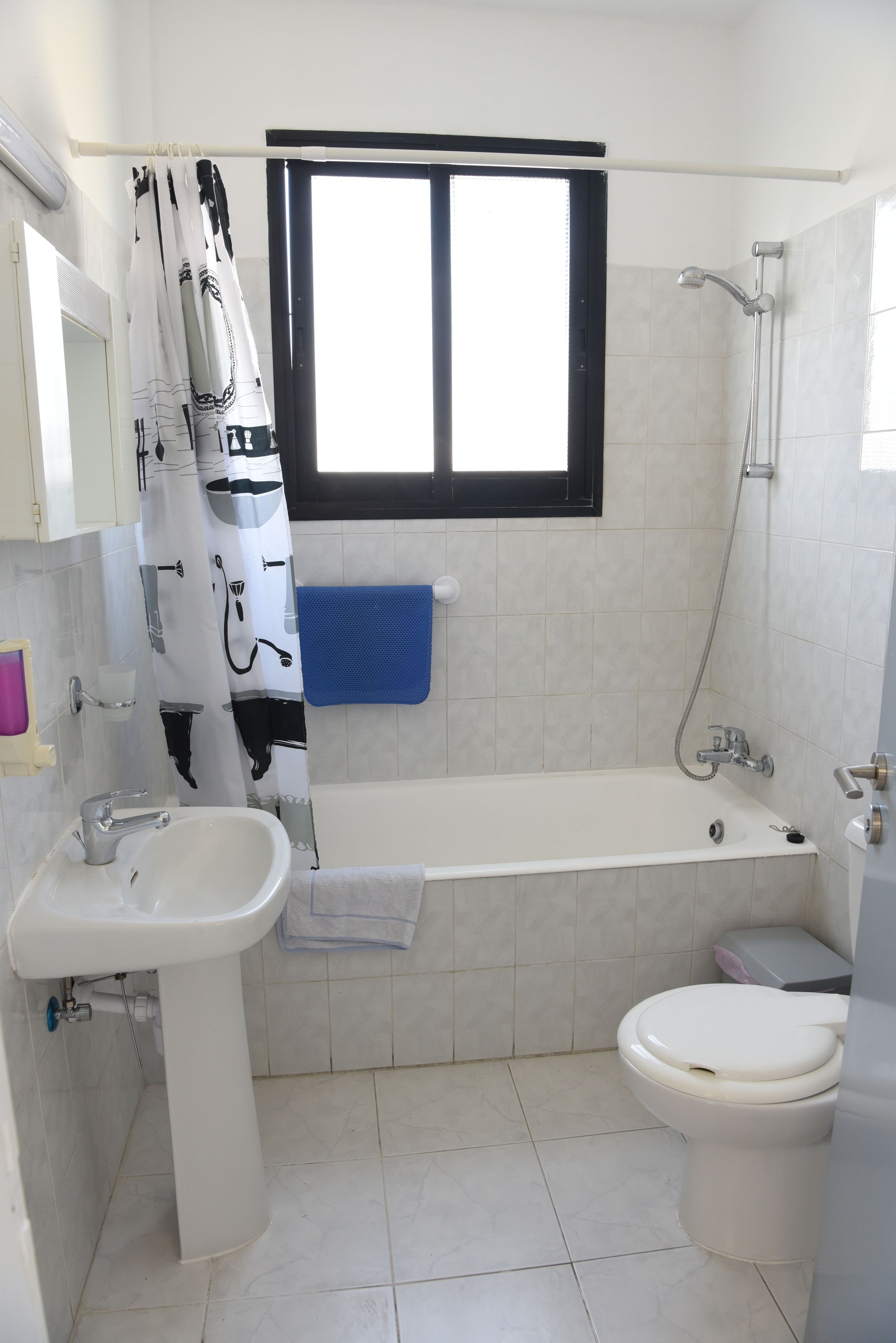 A bathroom with a bathtub, toilet, sink, and a window with a black frame.