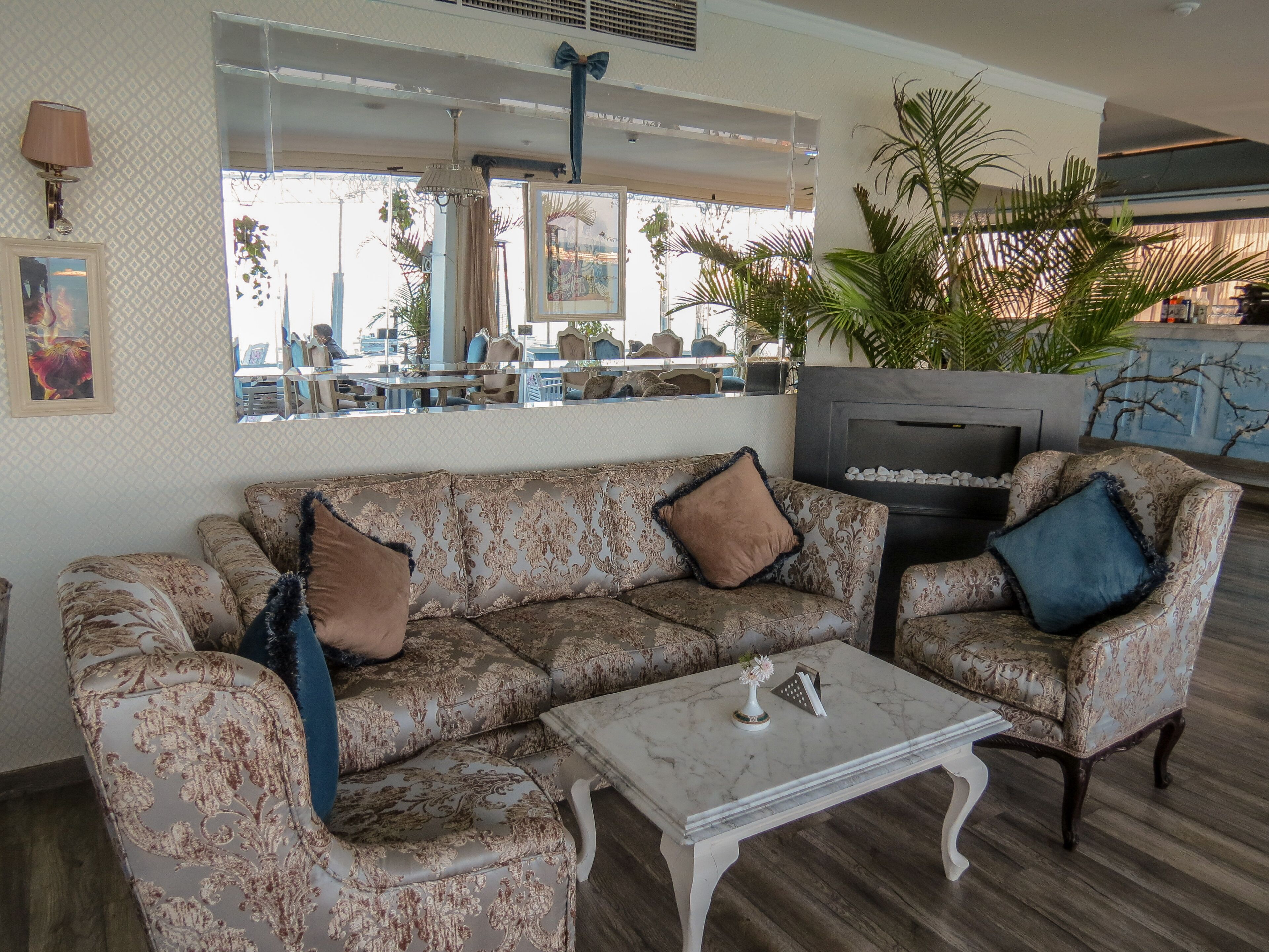 A living room with a patterned sofa, a marble coffee table, and a large mirror reflecting the outdoor area.