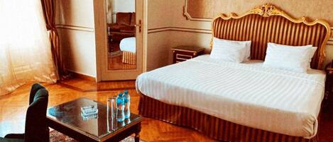 A hotel room with a large bed, a small table with water bottles, a chair, and a mirror.