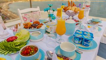 A breakfast table with various food items and drinks, overlooking a body of water.