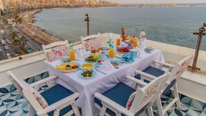 A table set for breakfast with a city view, including a coastal road and buildings in the background.