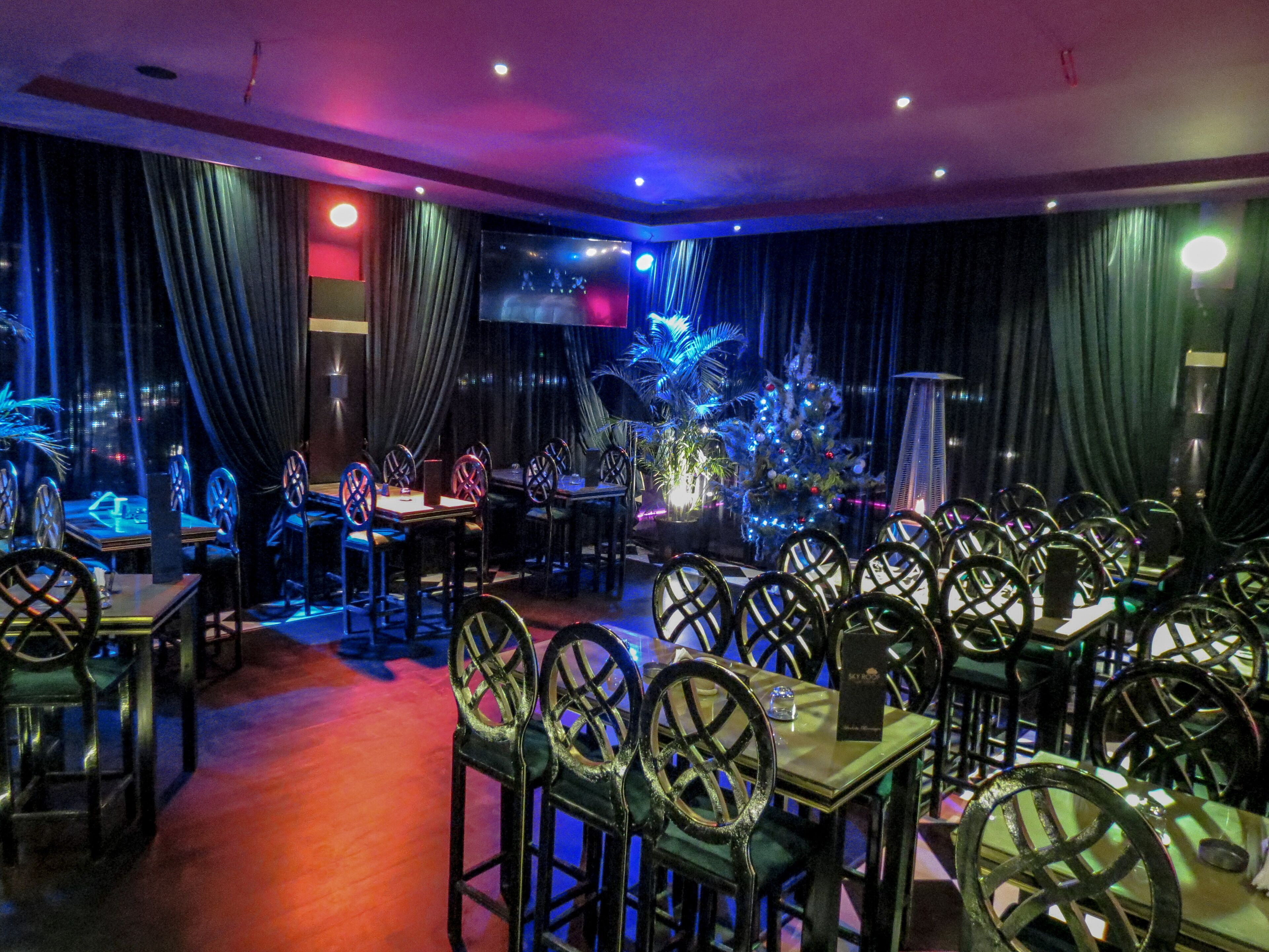 Un restaurante con mesas, sillas, un árbol de Navidad y cortinas.