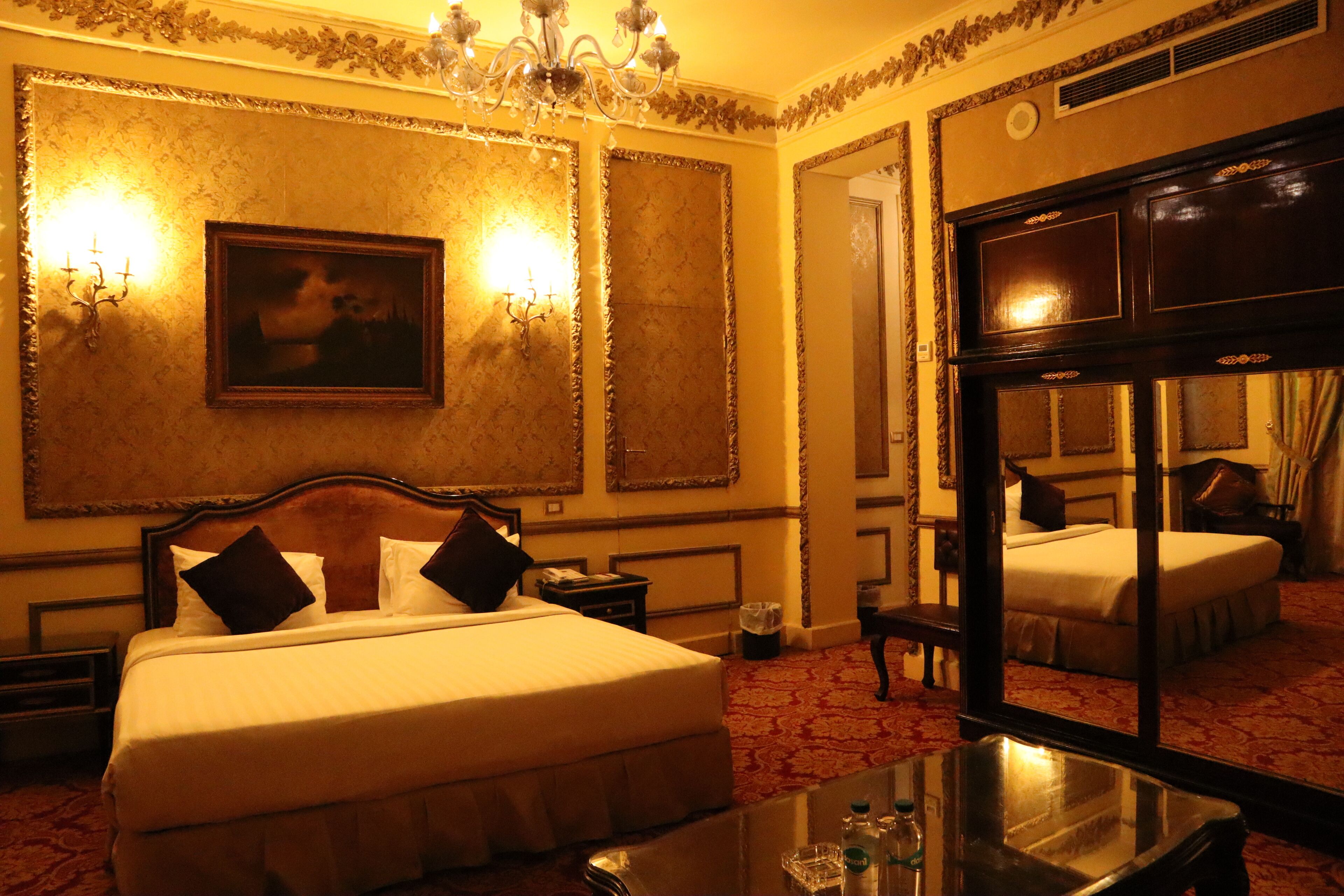 Une chambre d’hôtel avec un grand lit, une table de chevet, un miroir et un lustre.