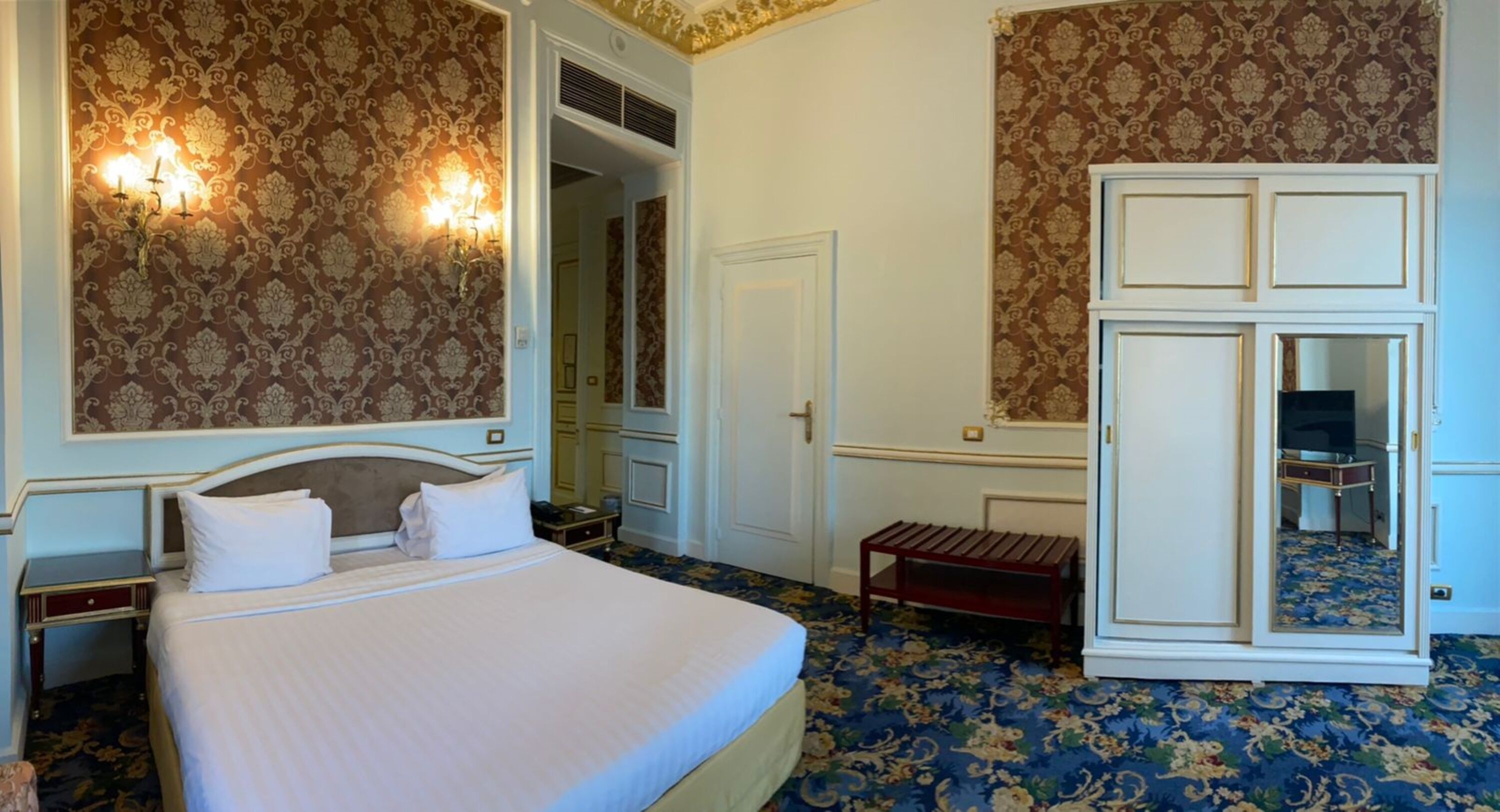 Een hotelkamer met een groot bed, een kledingkast, een klein bankje en een televisie.