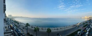A coastal cityscape with a wide road parallel to the sea, palm trees lining the road, and a clear sky. - Windsor Palace Luxury Heritage Hotel Since 1906 by Paradise Inn Group (Alexandria)