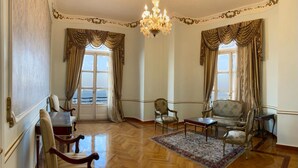 A spacious room with a wooden parquet floor, a chandelier, and classic furniture including a sofa, armchairs, and a table.