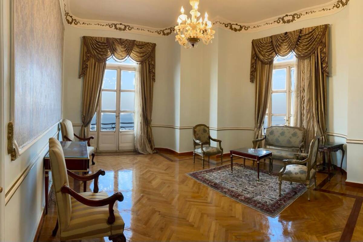 Amplia habitación con suelo de parqué de madera, una araña y muebles clásicos, incluyendo un sofá, sillones y una mesa.