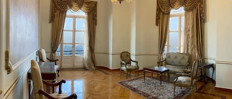 A spacious room with a wooden parquet floor, a chandelier, and classic furniture including a sofa, armchairs, and a table.