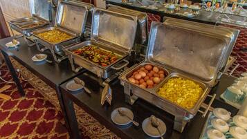 A buffet setup with various food items in metal containers, arranged on a table with a patterned carpet.