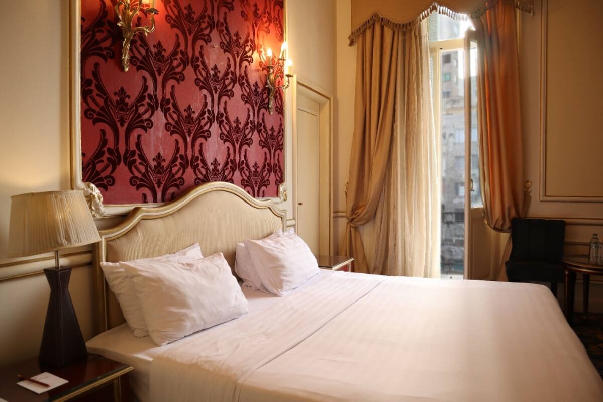Habitación de hotel con una cama grande, una mesita de noche con lámpara, una pared decorativa y vistas a través del ventanal.