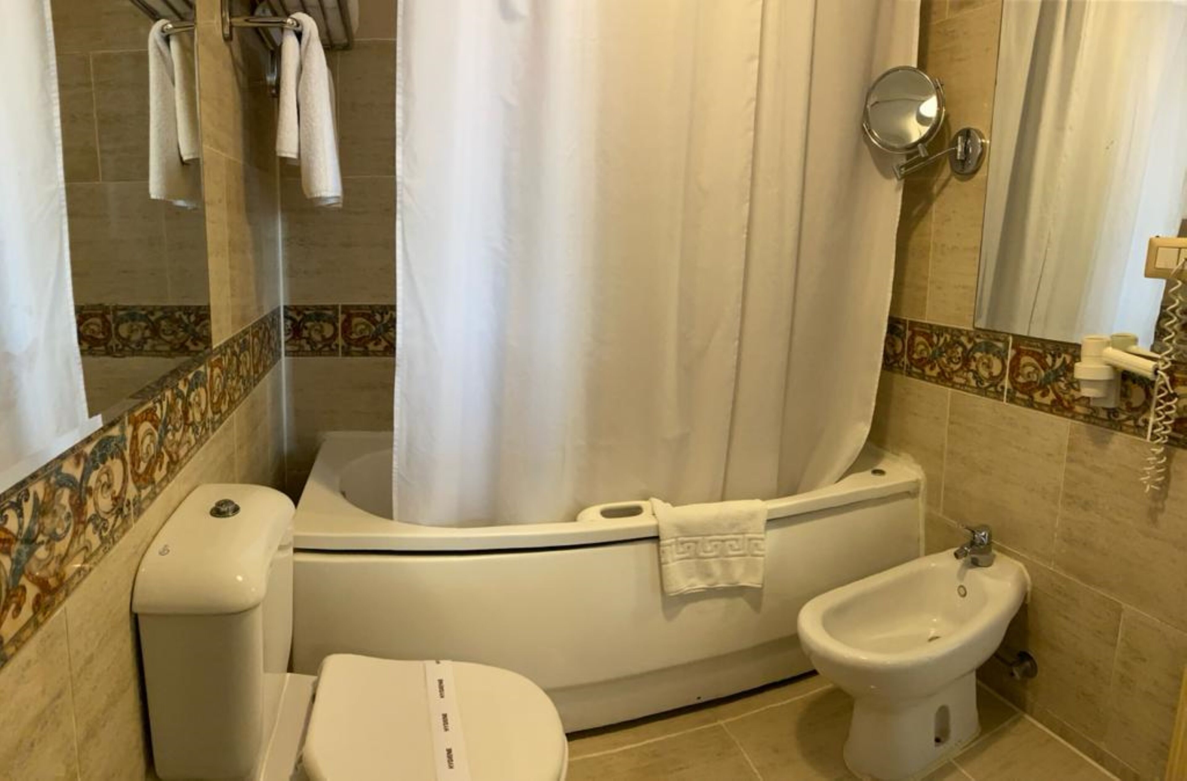 Un baño con bañera, inodoro, bidé y cortina de ducha.