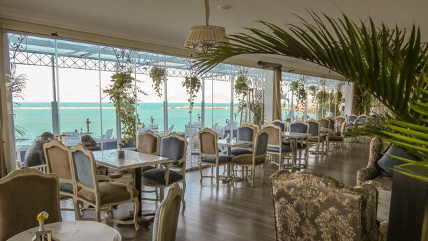 A restaurant with a view of the sea, featuring tables and chairs arranged for dining.