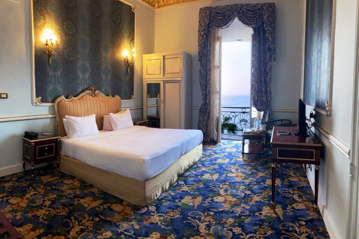 Habitación de hotel con una cama grande, un armario, un escritorio y vistas al mar desde un balcón.