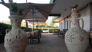 An outdoor patio with two large vases, tables, chairs, umbrellas, and a tiled floor. - Hotel Etna (Riccione)