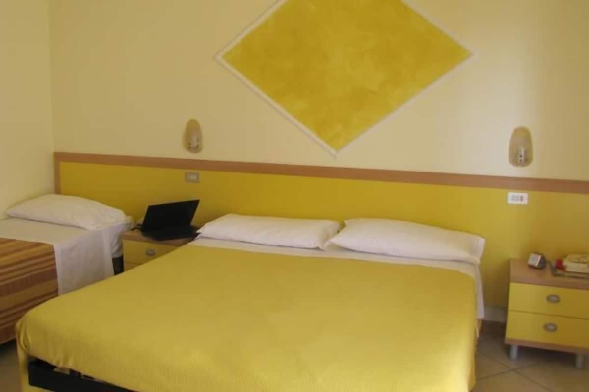 A hotel room with two single beds, a desk with a laptop, and a small bedside table with a lamp.